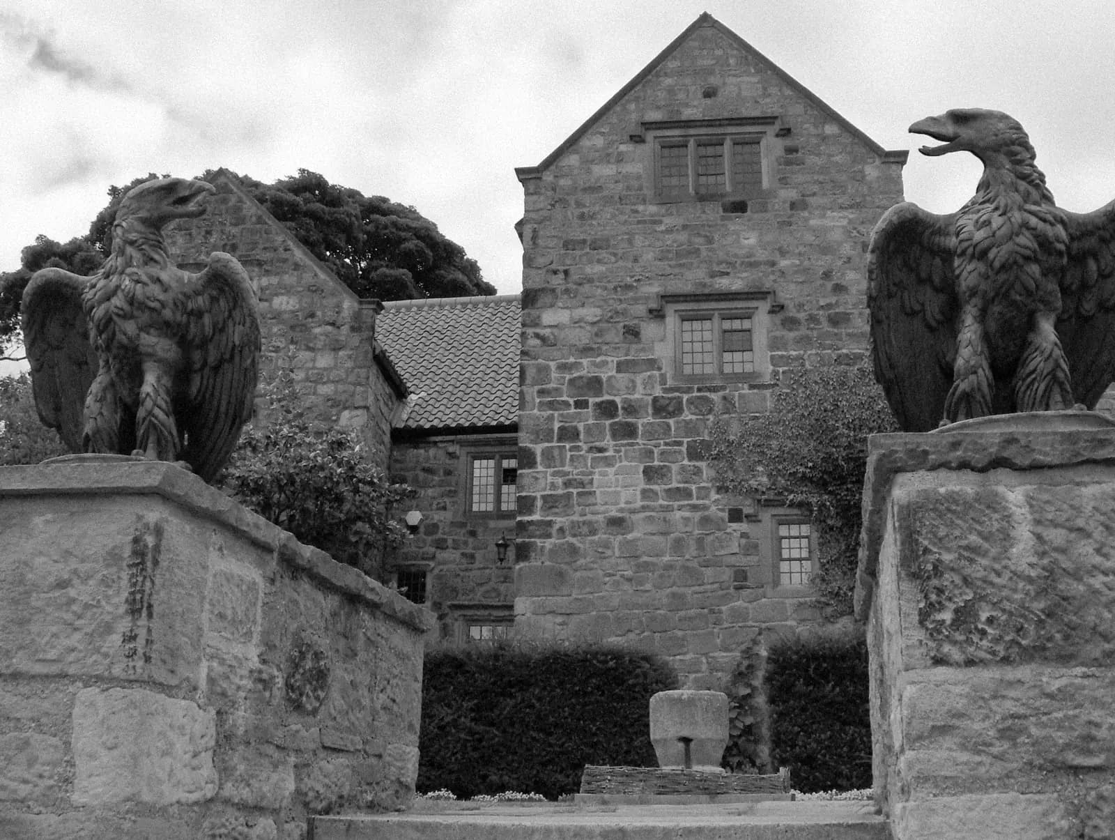 The stone gable of Washington Old Hall seen between two carved stone eagles on the gate piers.